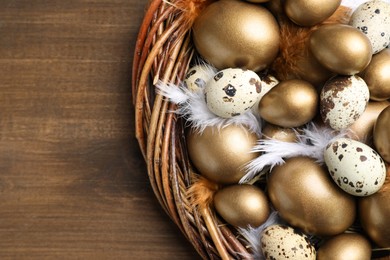 Many golden and quail eggs in nest on wooden table, top view. Space for text