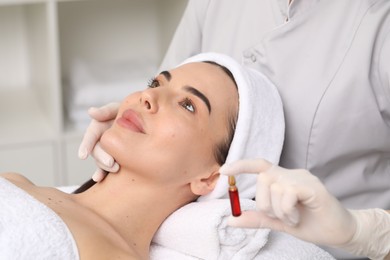 Professional cosmetologist holding skincare ampoule while working with client in clinic, closeup