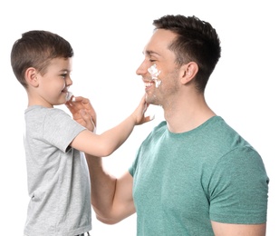 Dad and his little son applying shaving foam against white background