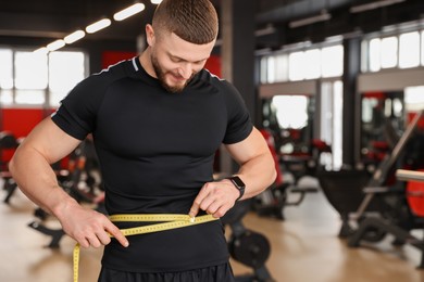 Photo of Athletic man measuring waist with tape in gym