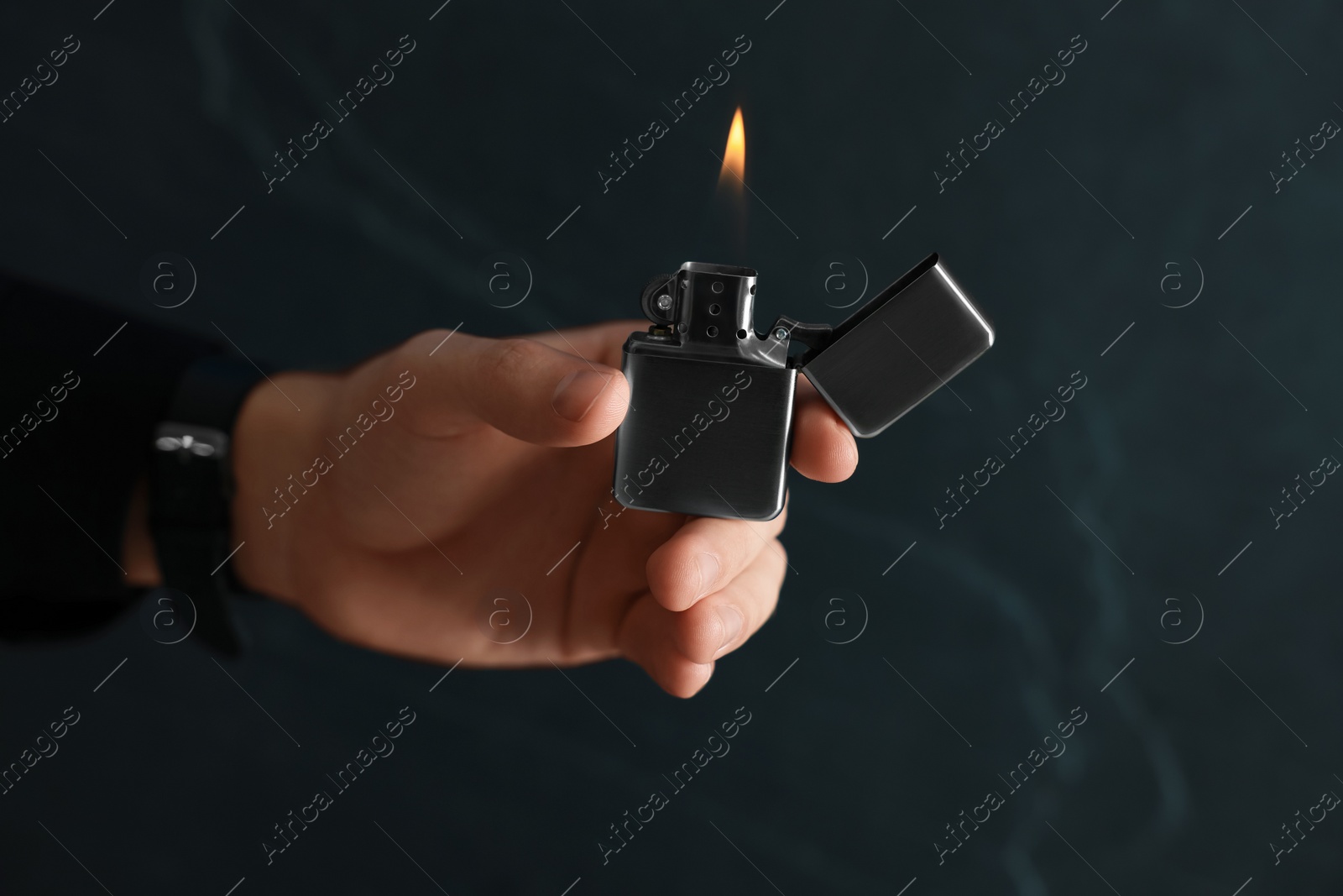 Photo of Man holding lighter with burning flame on dark background, closeup