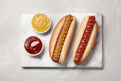 Photo of Fresh delicious hot dogs with sauces on light grey marble table, top view