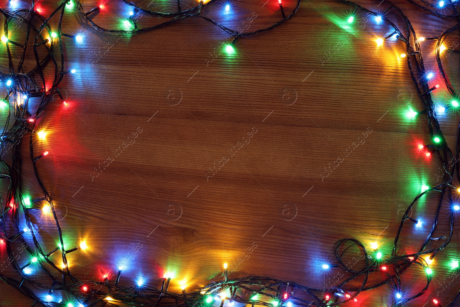 Photo of Frame of colorful Christmas lights on wooden table, top view. Space for text