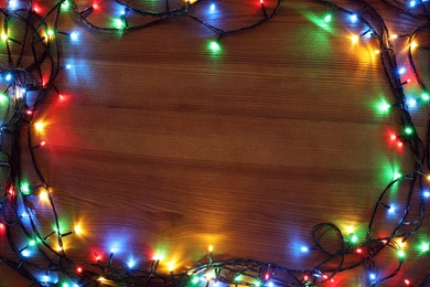 Frame of colorful Christmas lights on wooden table, top view. Space for text