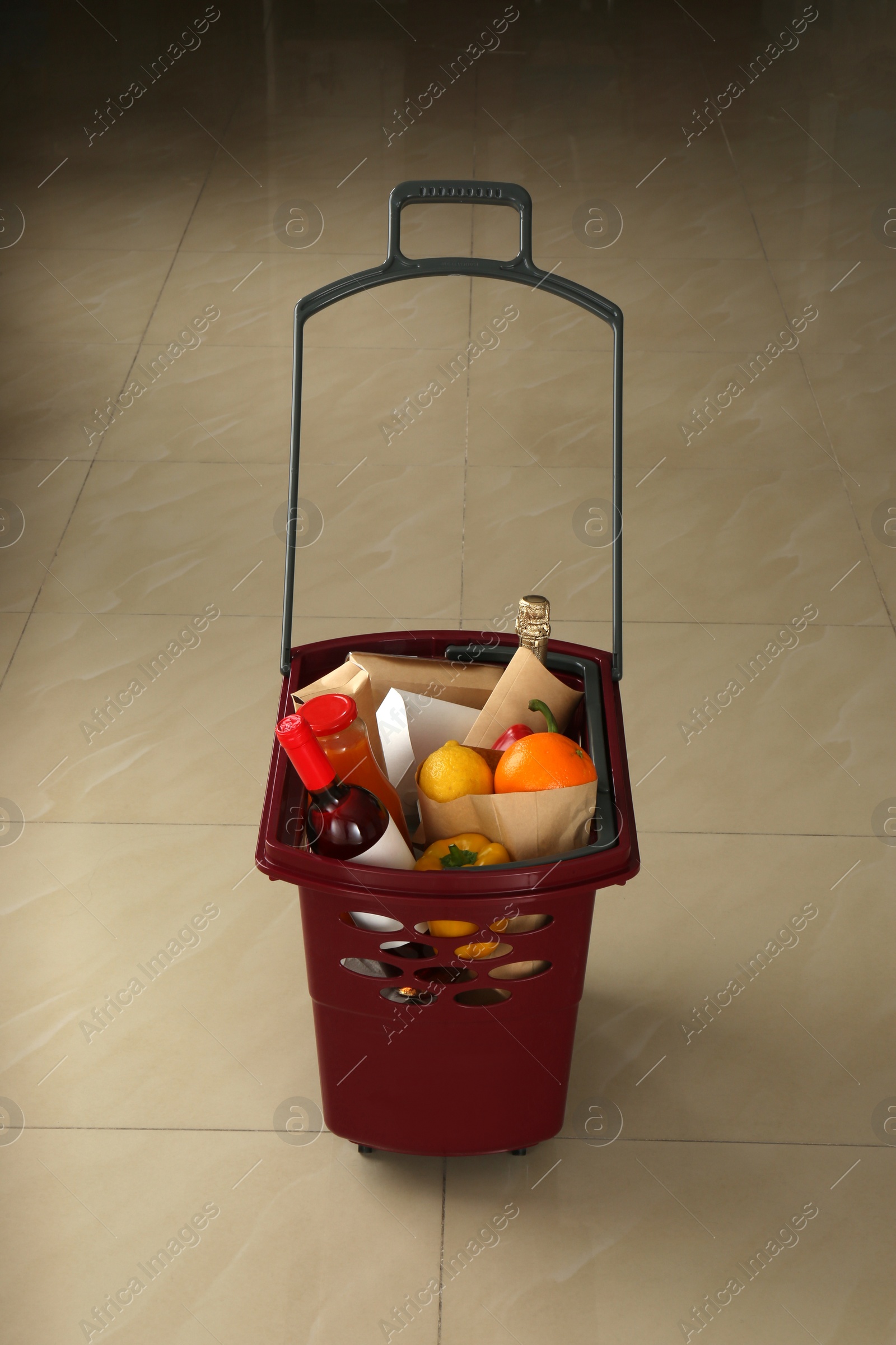 Photo of Shopping basket full of different products on beige tile floor