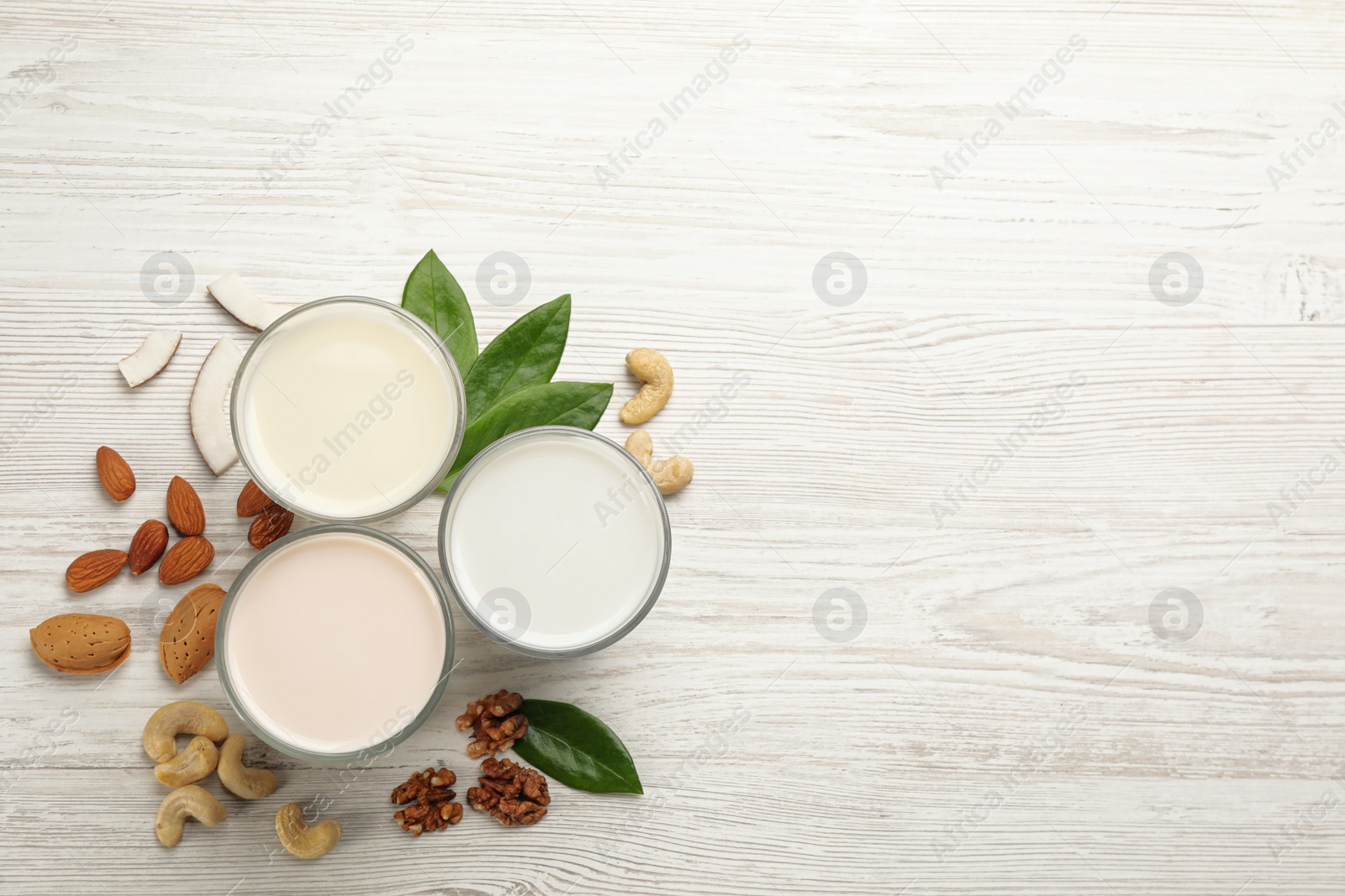 Photo of Different vegan milks and nuts on white wooden table, flat lay. Space for text