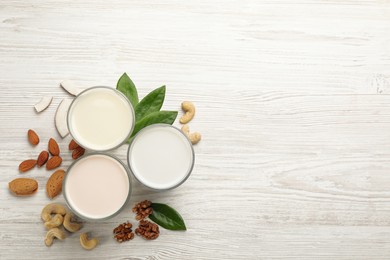 Different vegan milks and nuts on white wooden table, flat lay. Space for text