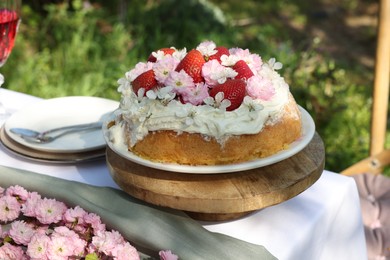 Photo of Delicious homemade cake decorated with fresh strawberries and spring flowers on table in garden