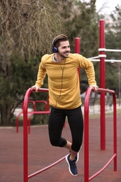 Young man with headphones listening to music and exercising on sports ground