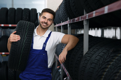 Photo of Male mechanic with car tire in auto store