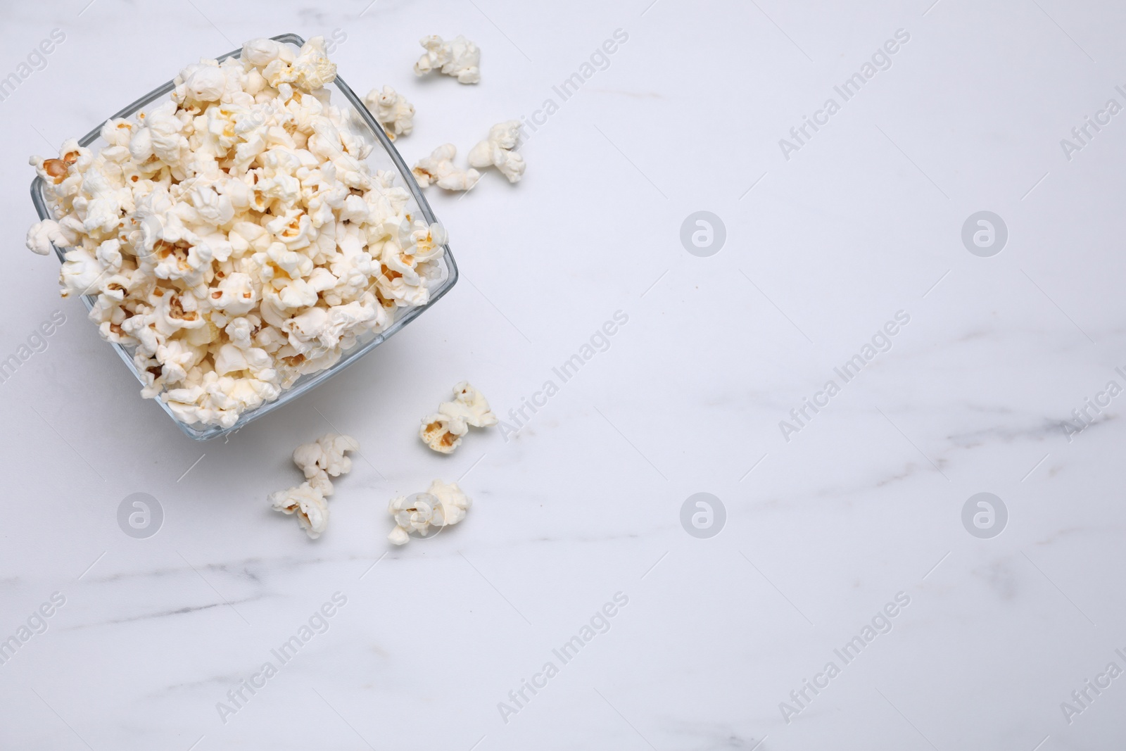 Photo of Bowl of tasty popcorn on white marble table, flat lay. Space for text