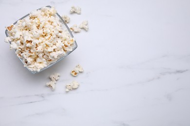 Photo of Bowl of tasty popcorn on white marble table, flat lay. Space for text