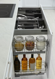 Photo of Open drawers with jars of food, wine bottles and utensils in kitchen