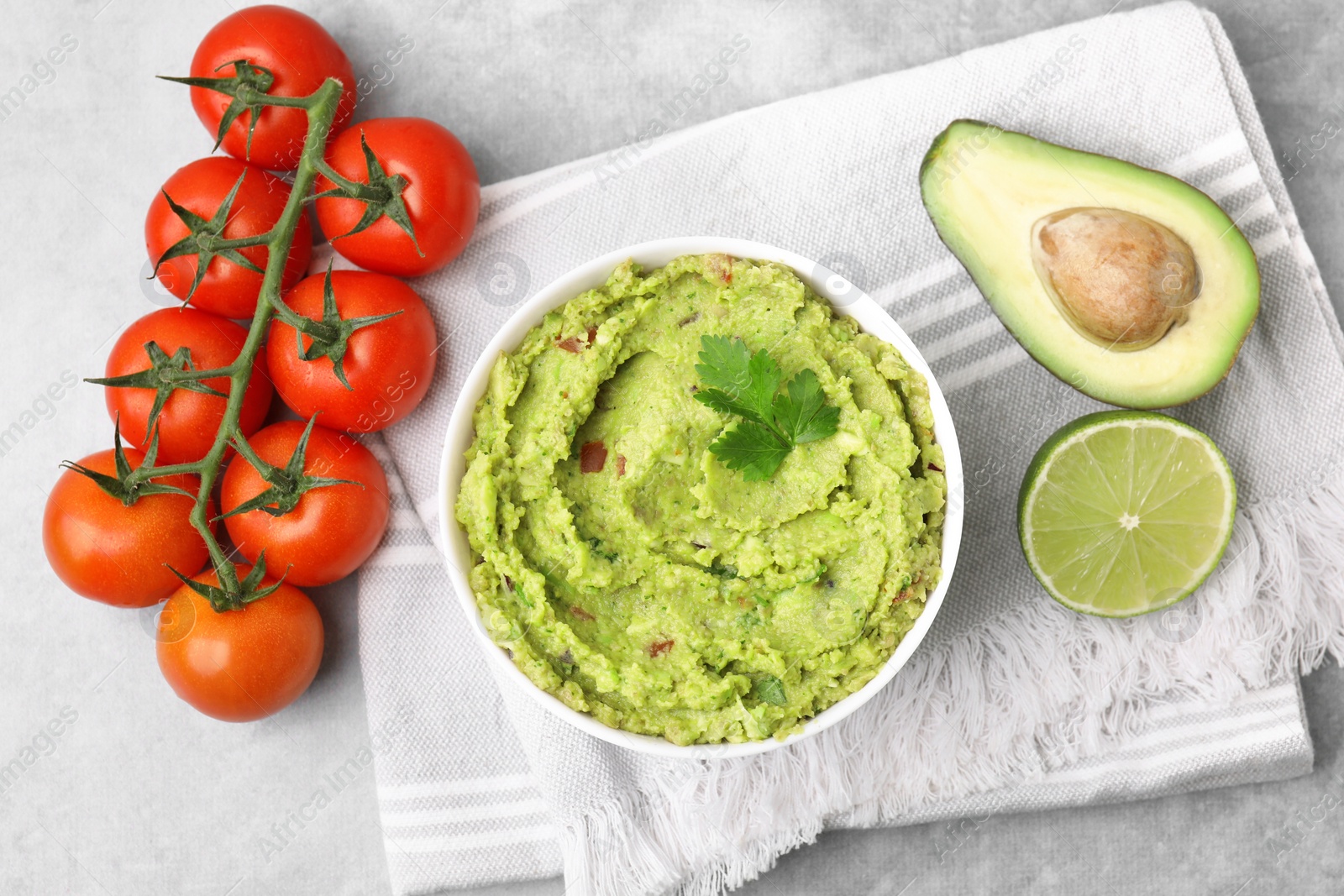 Photo of Bowl of delicious guacamole and ingredients on grey table, flat lay