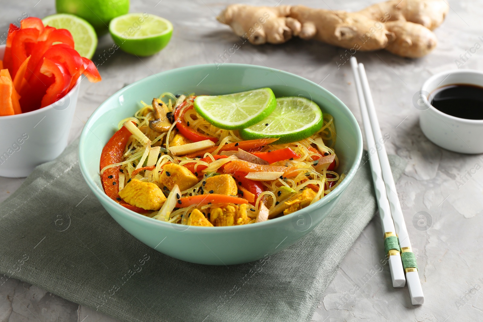 Photo of Stir-fry. Delicious cooked noodles with chicken and vegetables in bowl served on gray textured table