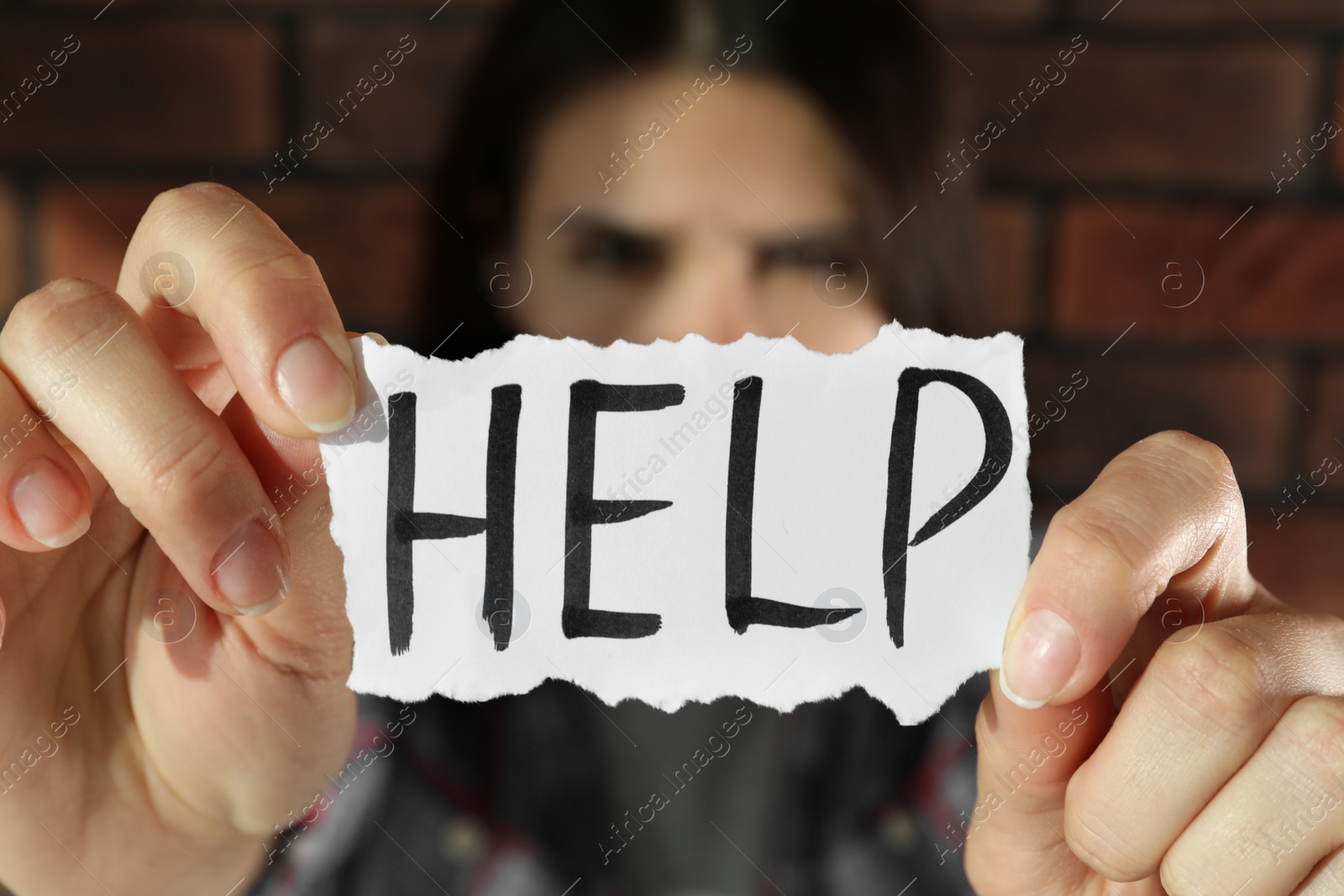 Photo of Domestic violence concept. Woman holding paper with written word Help near brick wall, focus on hands