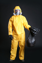 Photo of Man in chemical protective suit holding trash bag on black background. Virus research