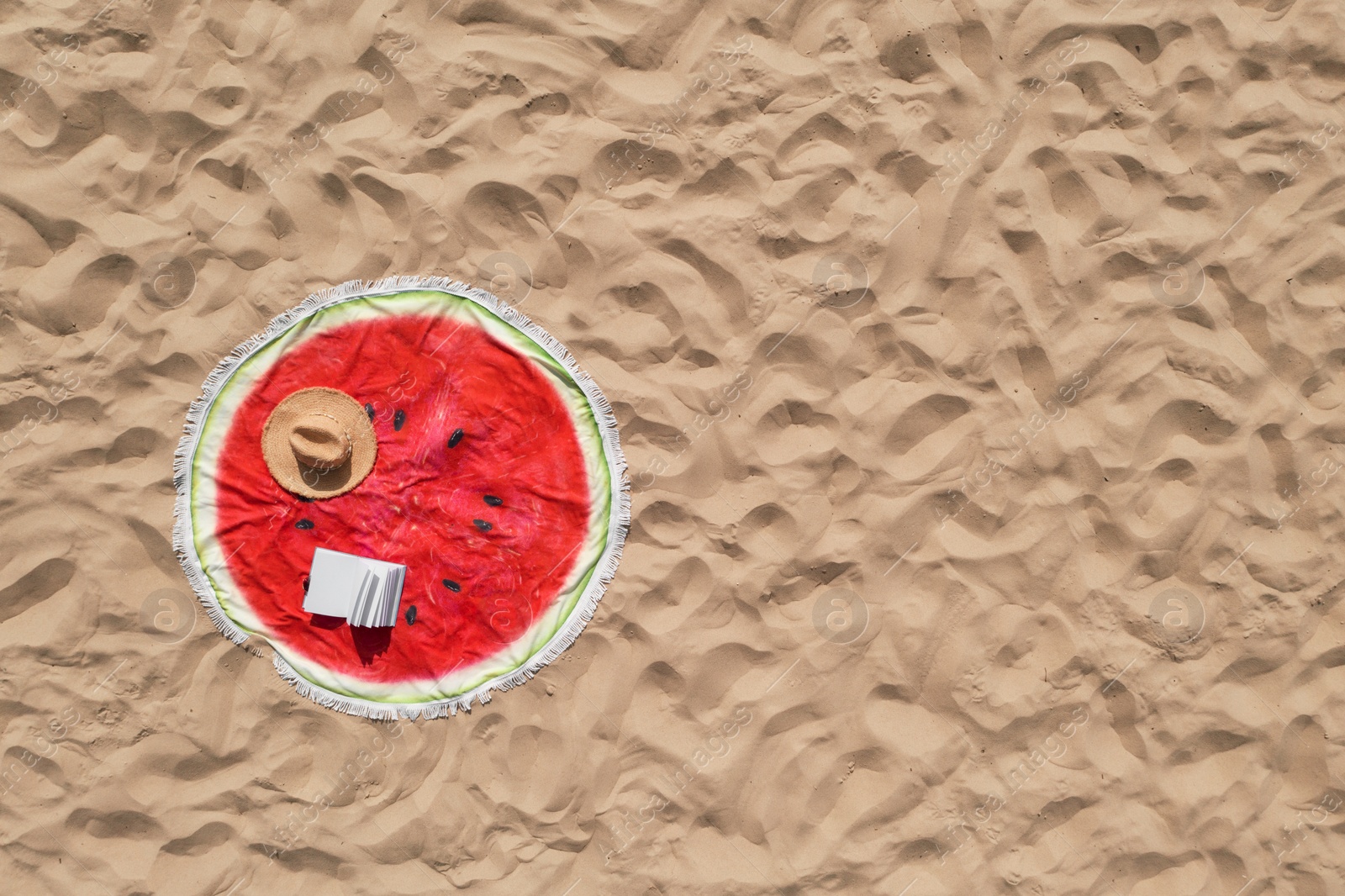 Image of Towel with book and straw hat on sandy beach, aerial top view. Space for text