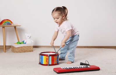 Cute little girl playing with drum, drumsticks and toy piano at home