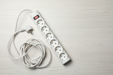 Photo of Power strip with extension cord on white wooden floor, top view. Space for text