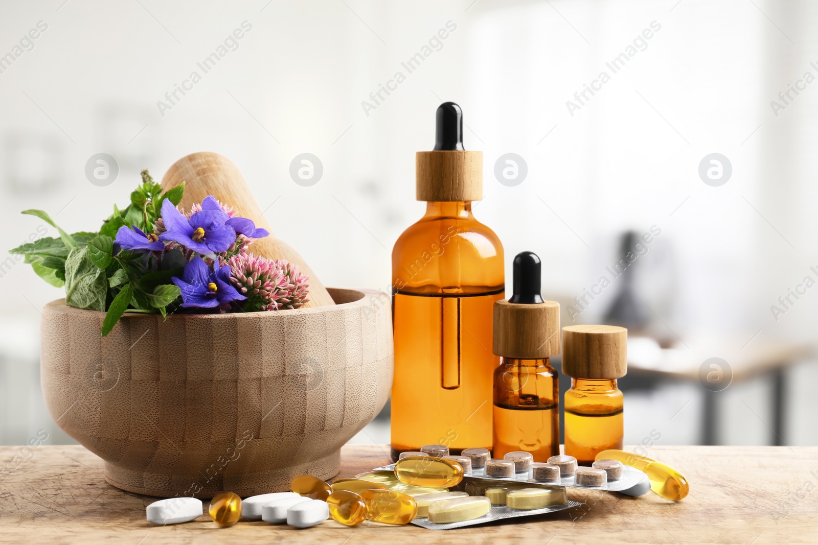 Image of Mortar with fresh herbs, bottles of extracts and pills on wooden table in medical office
