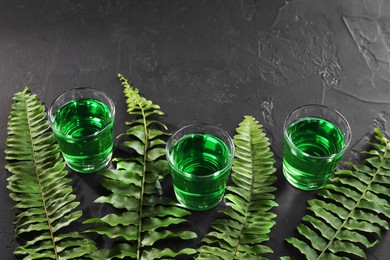 Photo of Absinthe in shot glasses and green leaves on black table, space for text. Alcoholic drink