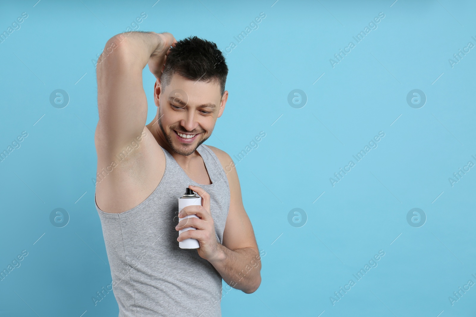 Photo of Handsome man applying deodorant on turquoise background. Space for text