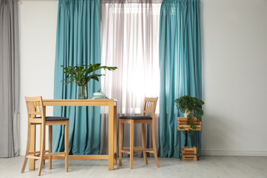 Stylish wooden table and chairs near window with elegant curtains in room