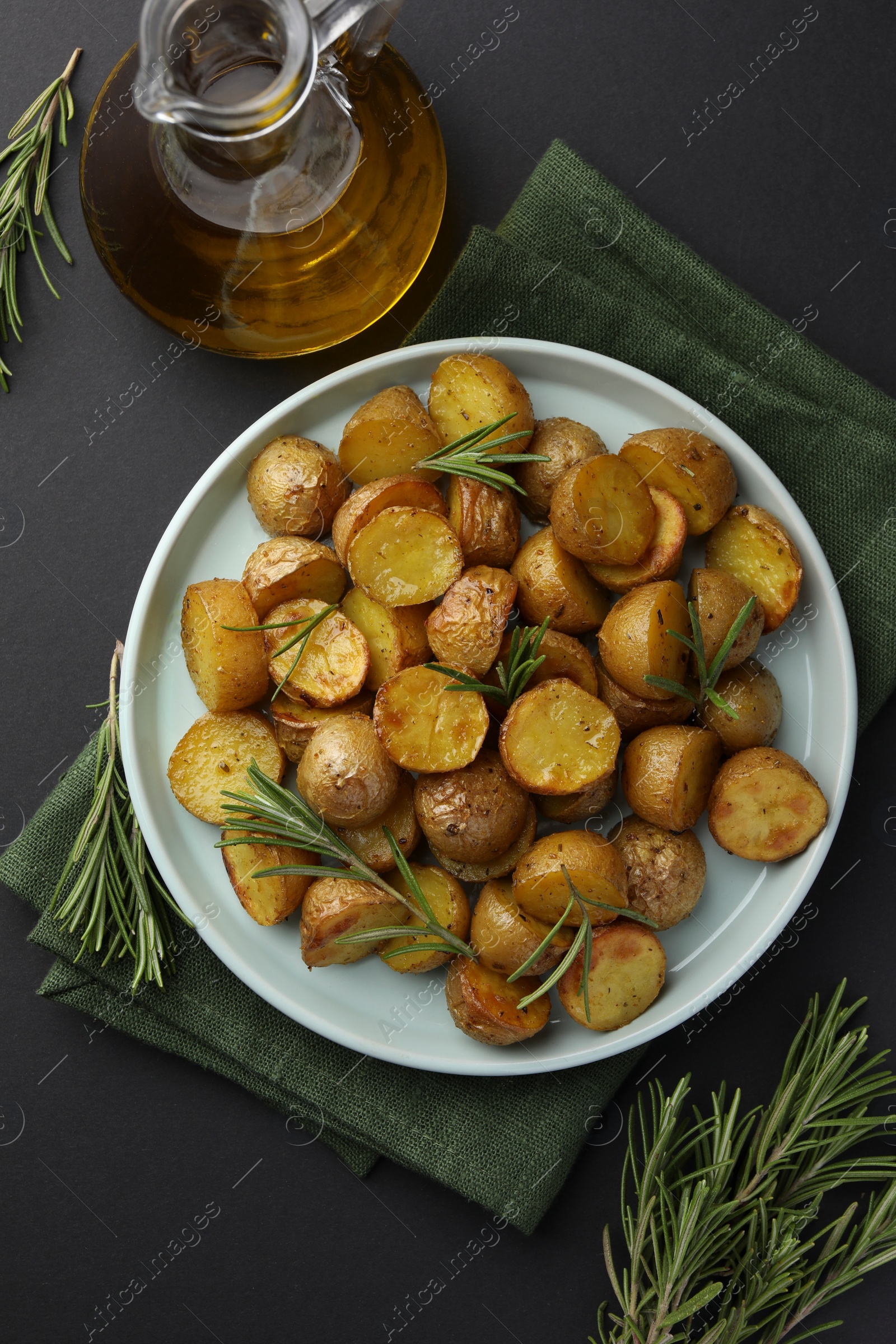 Photo of Delicious baked potatoes with rosemary and oil on black table, flat lay