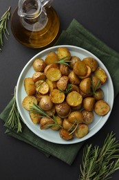 Delicious baked potatoes with rosemary and oil on black table, flat lay