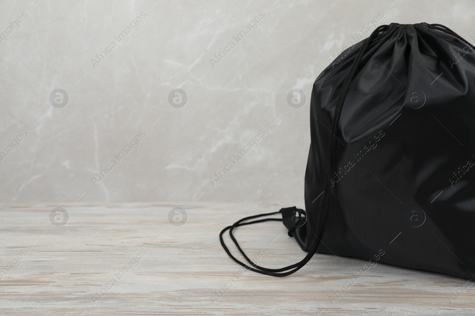 Photo of Black drawstring bag on light wooden table. Space for text