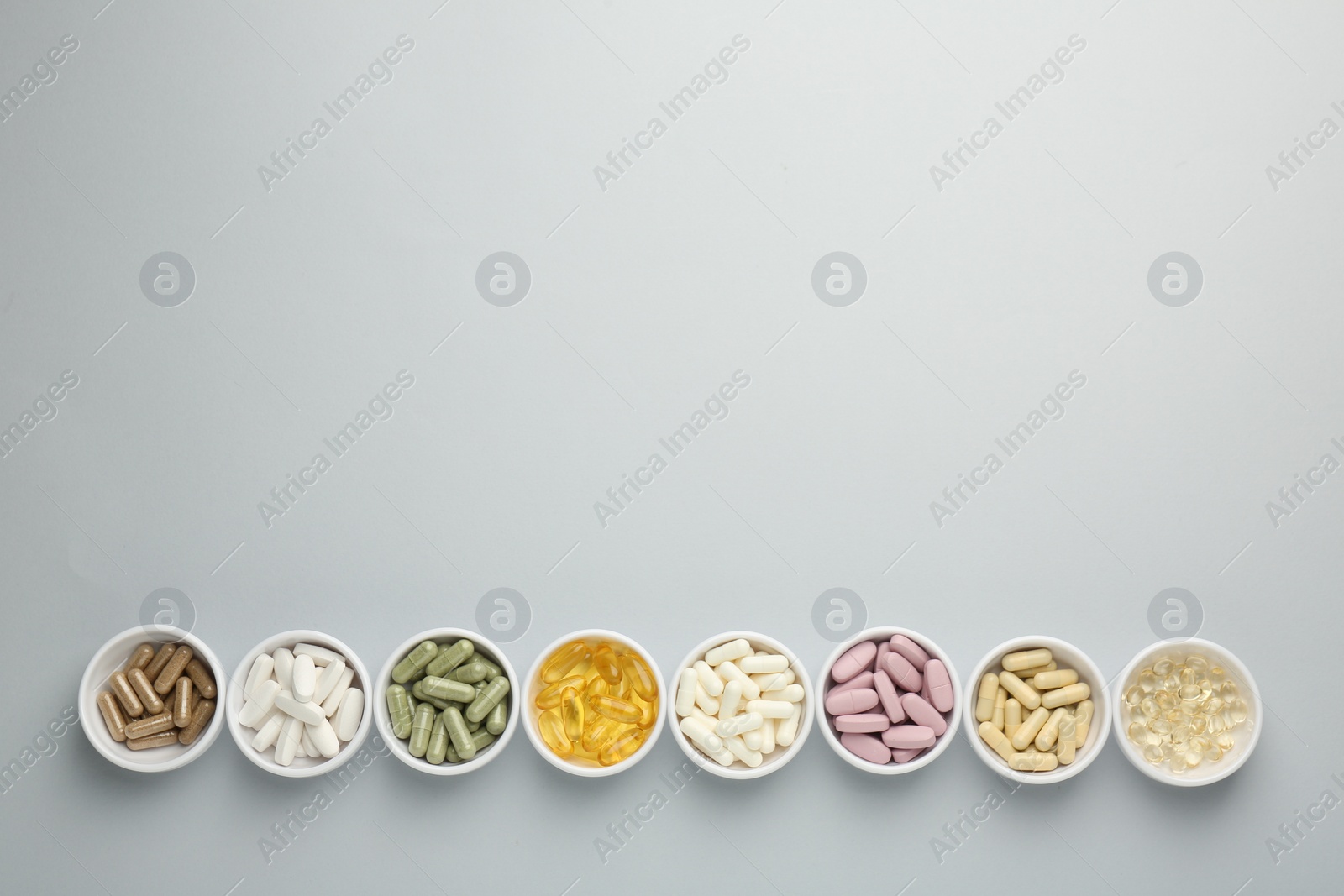 Photo of Different vitamin pills in bowls on grey background, flat lay. Space for text