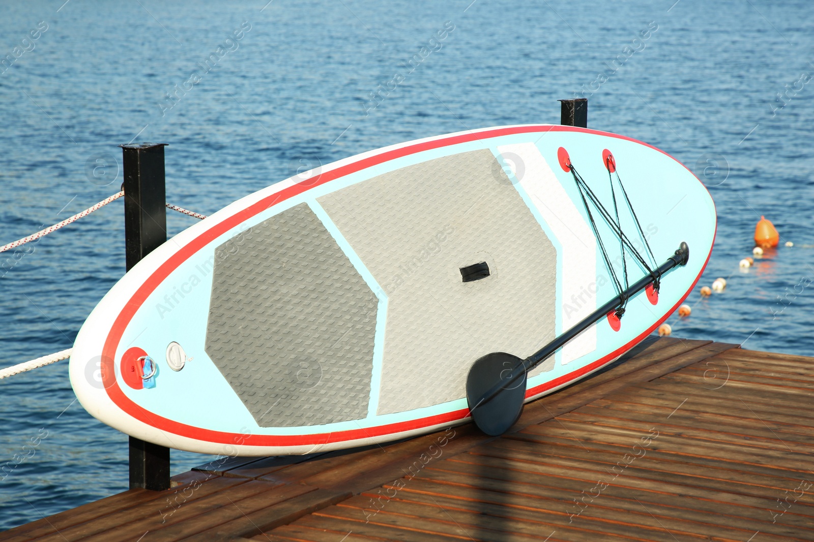 Photo of SUP board with paddle on wooden pier near sea