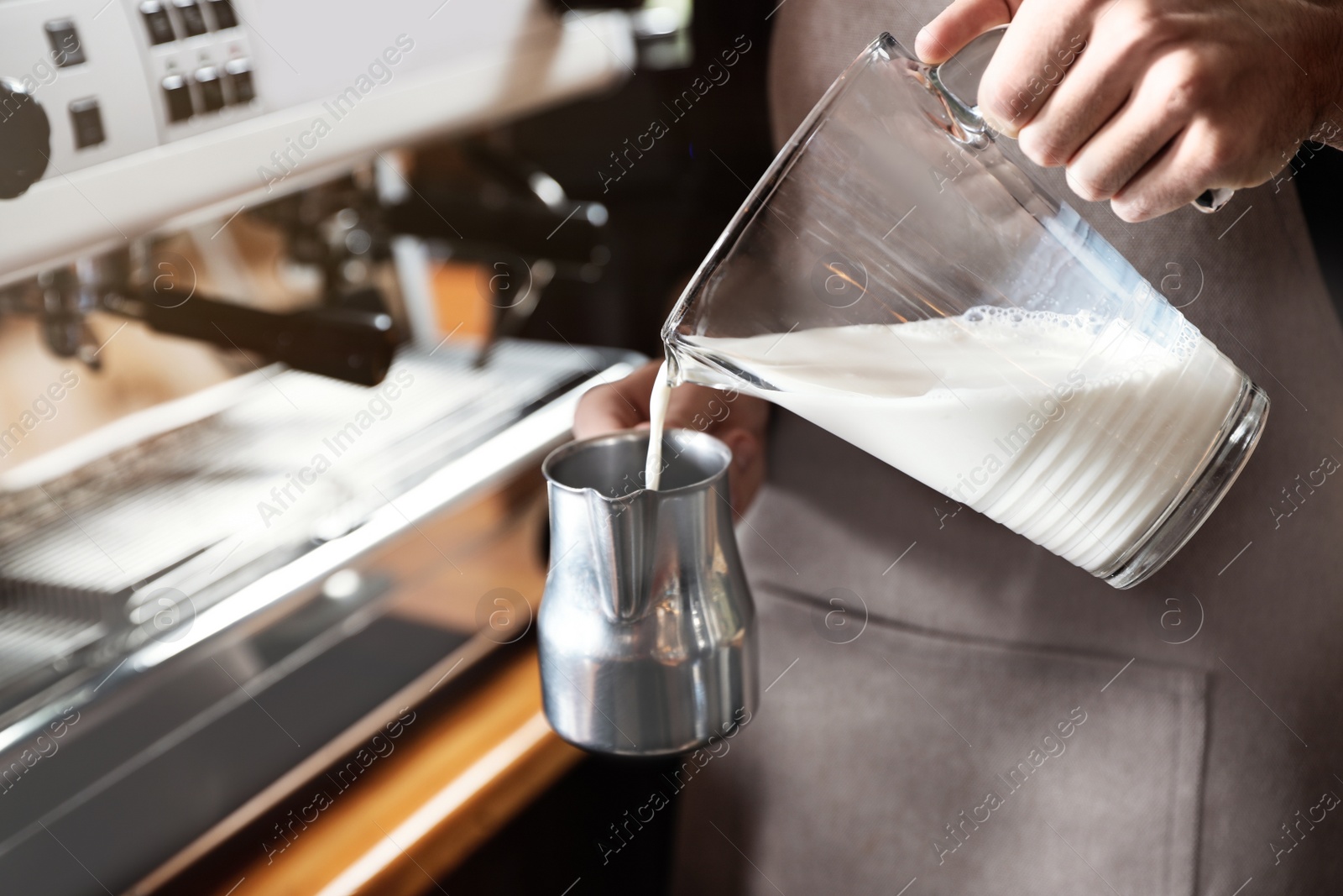 Photo of Barista pouring milk into metal pitcher indoors, closeup. Coffee making