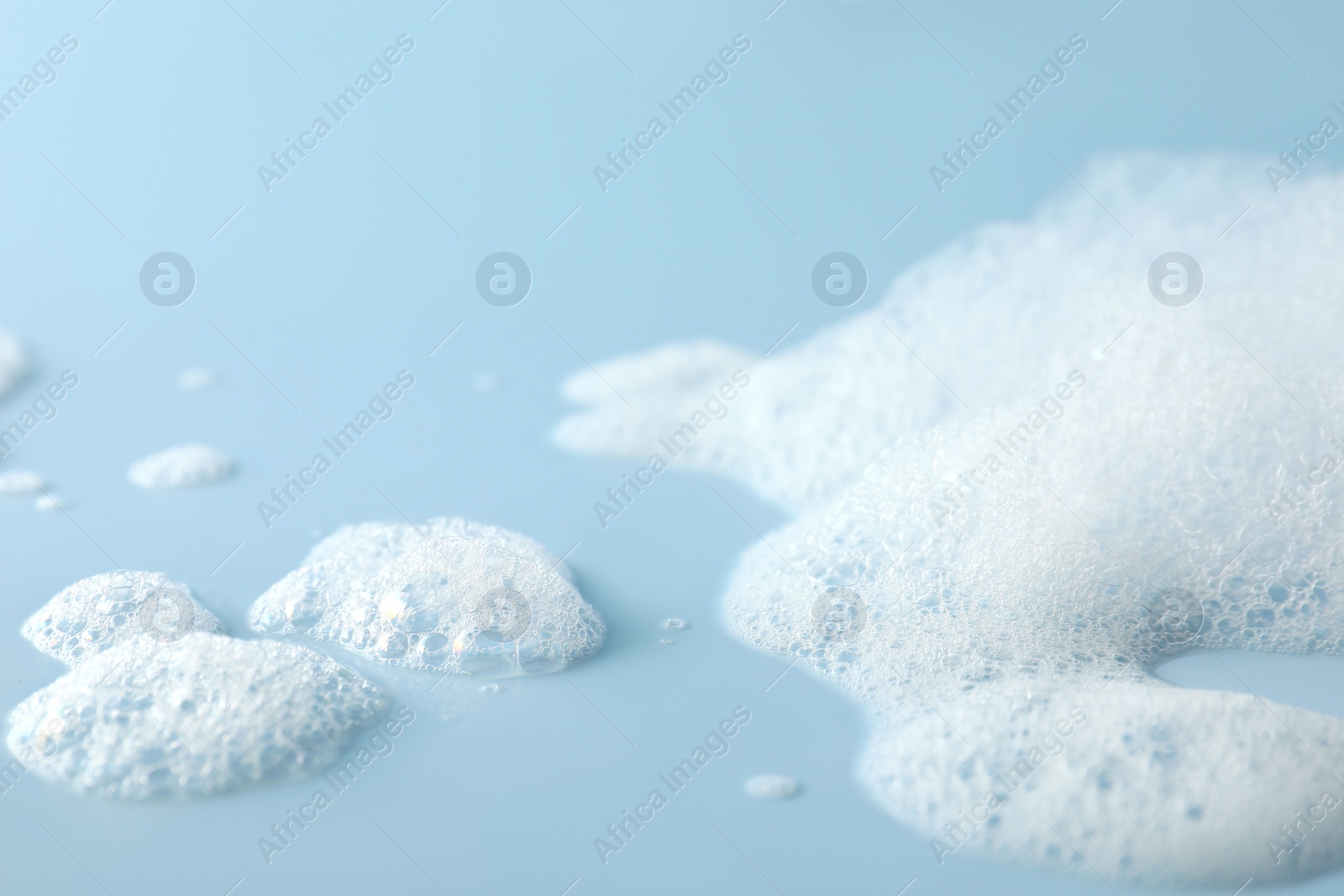 Photo of Fluffy bath foam on light blue background, closeup