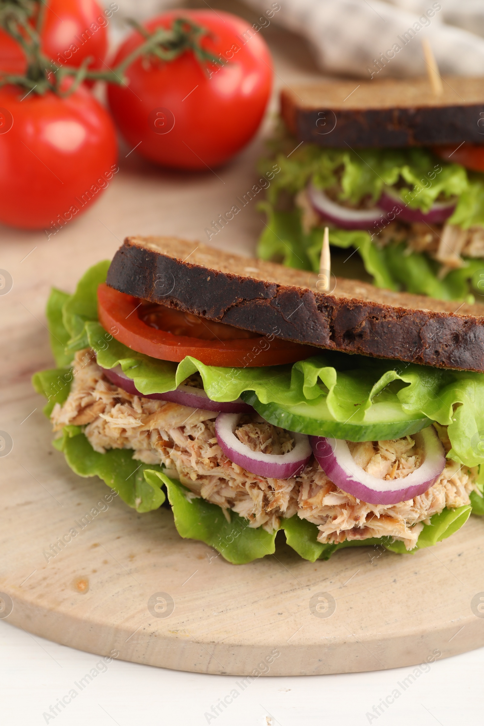 Photo of Delicious sandwiches with tuna and vegetables on wooden serving board, closeup