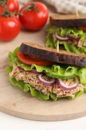 Photo of Delicious sandwiches with tuna and vegetables on wooden serving board, closeup