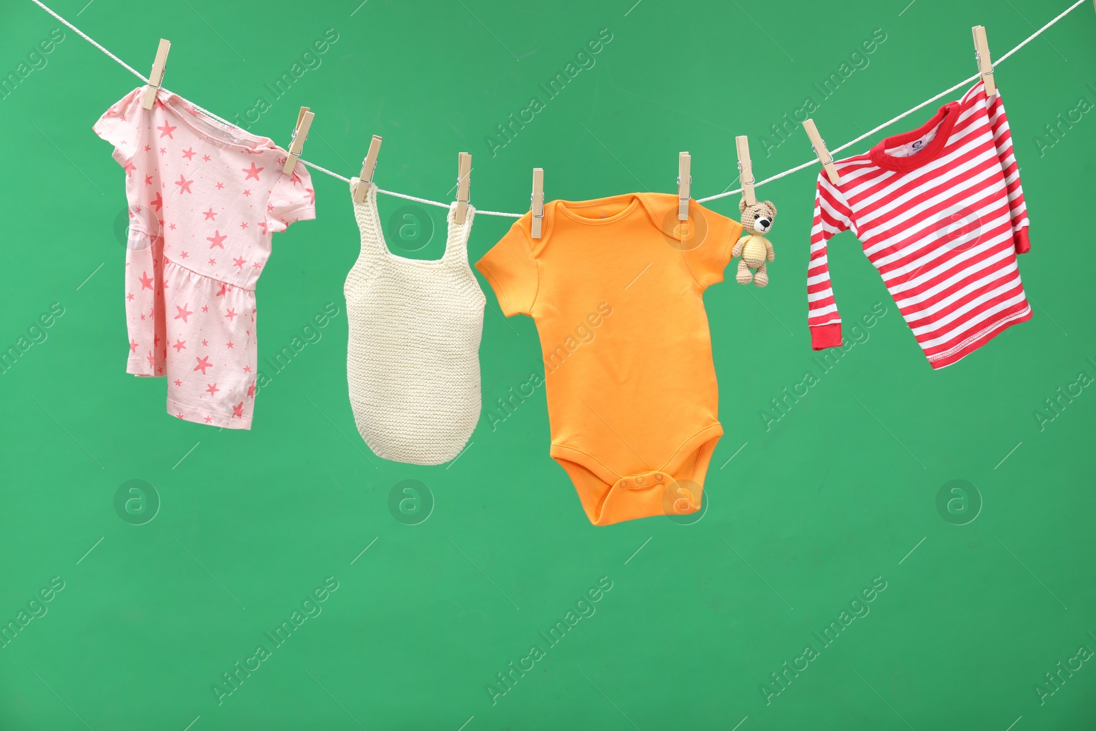 Photo of Different baby clothes and bear toy drying on laundry line against green background