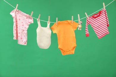 Photo of Different baby clothes and bear toy drying on laundry line against green background