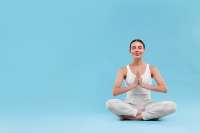 Photo of Beautiful young woman practicing yoga on light blue background, space for text. Lotus pose