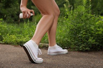 Woman applying insect repellent onto leg in park, closeup. Tick bites prevention