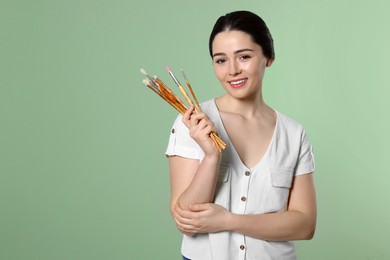 Woman with paintbrushes on pale green background, space for text. Young artist