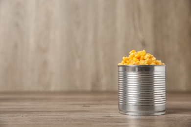 Photo of Open tin can of sweet corn on wooden table, space for text