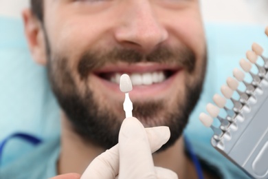Photo of Dentist matching young man's teeth color with palette, closeup