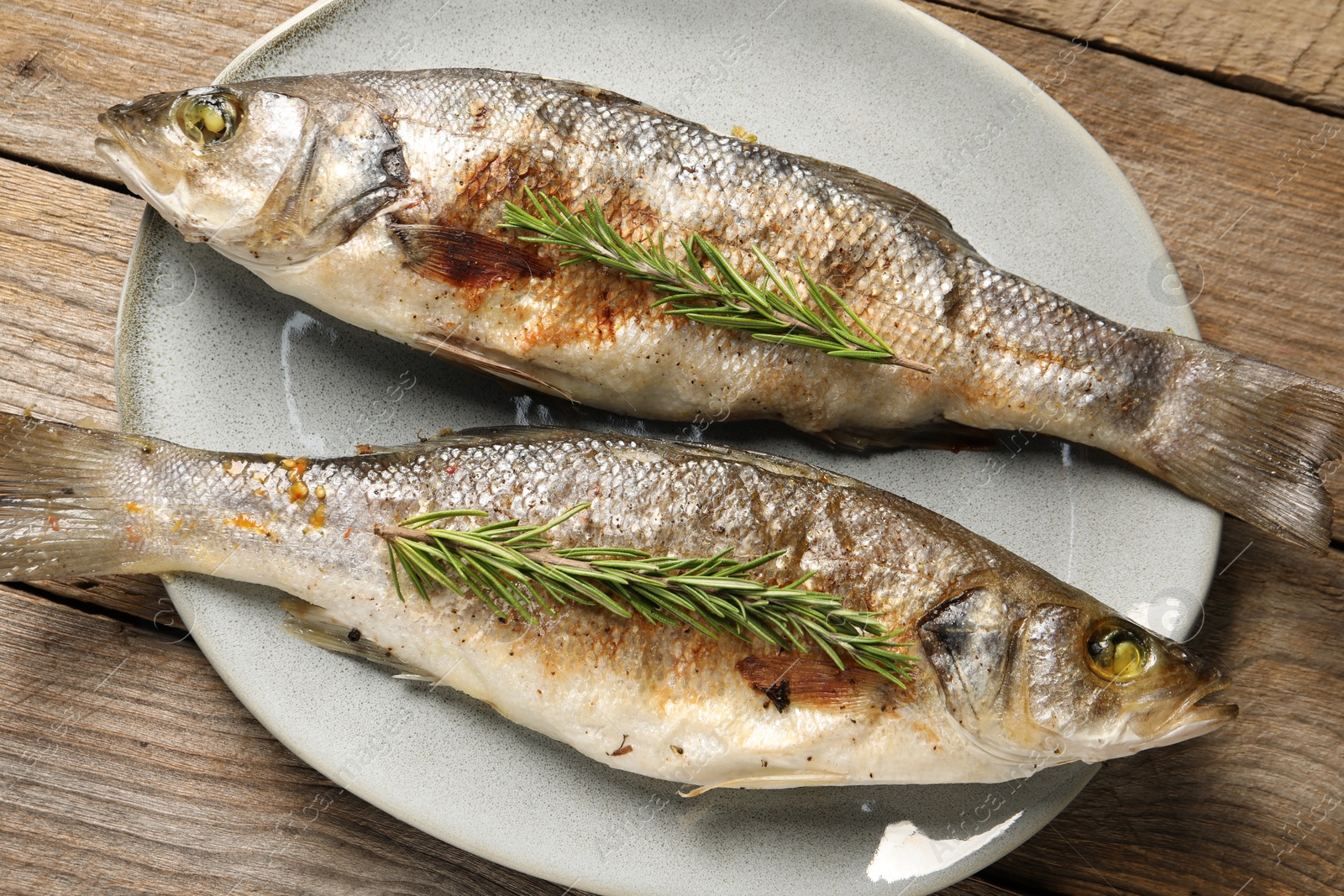 Photo of Delicious baked fish and rosemary on wooden table, top view