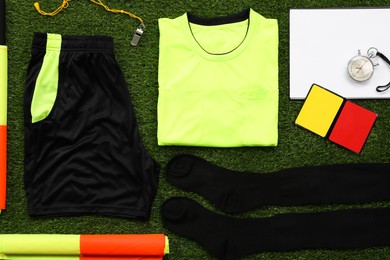 Photo of Uniform and other referee equipment on green grass, flat lay