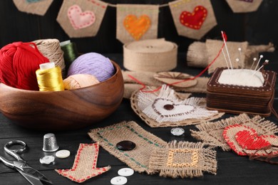 Photo of Pieces of burlap fabric with different stitches, scissors, threads, thimble and buttons on black table, closeup