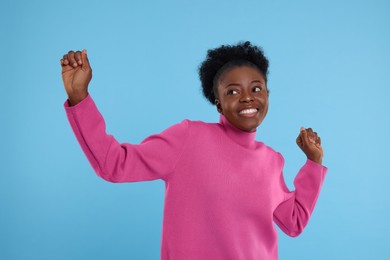 Happy young woman dancing on light blue background