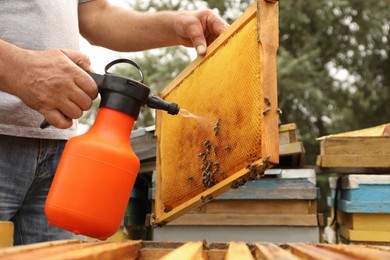 Photo of Beekeeper spraying sugar water onto frame with bees at apiary, closeup. Harvesting honey