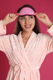 Photo of Beautiful young woman in bathrobe and eye sleeping mask on crimson background